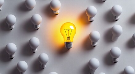 A single illuminated yellow light bulb standing out among many unlit white light bulbs on a gray surface symbolizing uniqueness and creativity