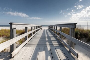 Fototapeta premium wooden boardwalk stretching towards a sandy beach with sea grass under a bright blue sky with scattered clouds