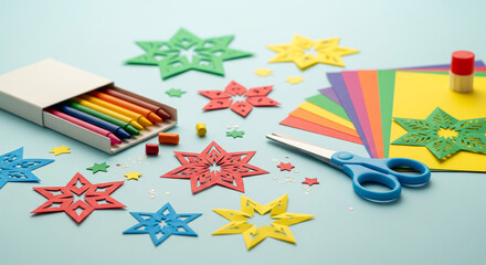 Creative DIY arts and crafts activity with colorful paper star decorations, wax crayons, scissors, and a glue stick on a pastel blue surface