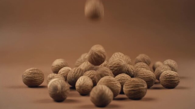 Hands dropping whole nutmegs onto a brown background creating a pile