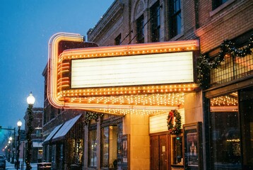 A vintage theater marquee illuminated at night. The building features classic architecture with decorative elements. Snow is visible on the ground, creating a winter atmosphere. christmas