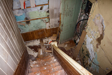 Dilapidated interior view of an old abandoned house staircase with peeling paint and scattered debris, capturing decay and neglect