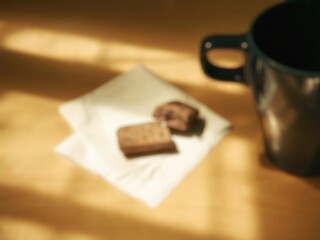 Blurred image of a simple aesthetic breakfast menu. Blurred image of a cup and a piece of chocolate biscuit on a table with patterned sunlight.