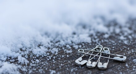 Fototapeta premium Silver safety pins for race bibs lying on a snow-dusted wooden surface, symbolizing winter marathon race preparation concept and endurance