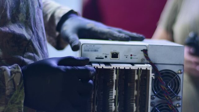 Hands dissambly Cryptocurrency Miner with printed circuit board (PCB) on top with network (Ethernet) ports and other control connectors and Multiple heatsinks and fans