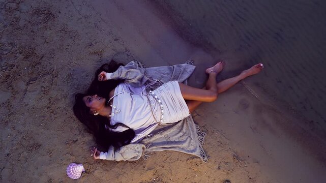 Aerial shot of a woman lying on a moonlit beach at night, embracing tranquility and solitude