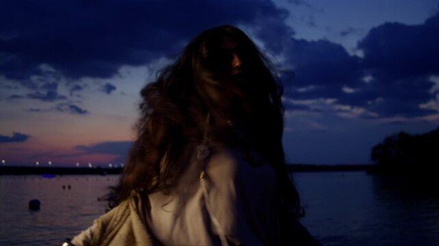 Woman performs a mystical dance performance under a dramatic twilight sky with expressive gestures and jewelry