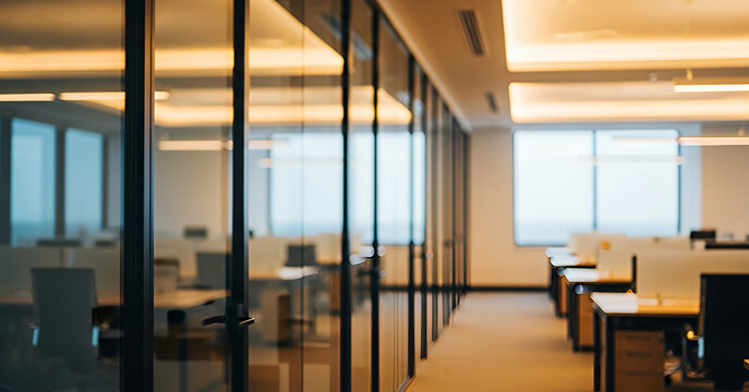 Warm interior lighting highlights the modern layout of an open office, where clear glass rooms and aligned desks contribute to a refined and efficient workspace design. - Powered by Adobe