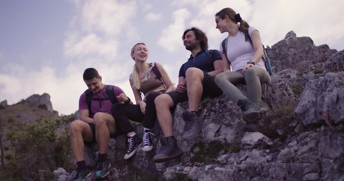 Four friends sit atop a rock, sharing vibrant conversations and joyful laughter during a break on their nature hike. A perfect blend of friendship and adventure.