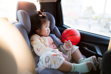 A cute little Asian girl sits hugging a basketball on the backseat of a car during a trip,Smiling...