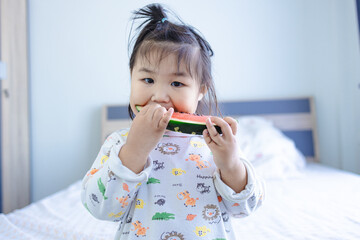 A cute little Asian girl is biting a watermelon,young girl eating watermelon against real kitchen background