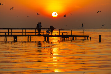 Silhouette of tourists watching the sunrise in the morning on a wooden bridge with seagulls flying around,Seagulls Beautiful sunset sky birds flying in Thailand background happiness calm nature clound