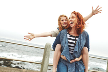 Ocean, piggyback and mother with girl, funny and nature with relationship, holiday and humor. Happy family, parent and mama carrying daughter, smile and bonding together with vacation, love and beach