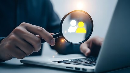 Close-up shot of a person's hands using a magnifying glass to examine a digital representation of people icons on a laptop screen