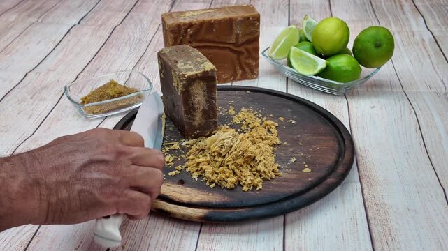 Hand scraping traditional Venezuelan panela on board with fresh limes nearby
