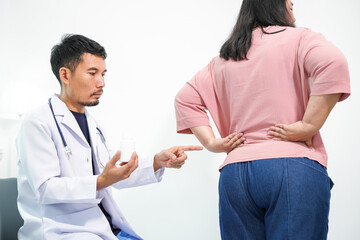 An Asian female patient receives a medical examination from a specialist focusing on low back pain. The doctor provides a thorough assessment and supportive advice in a calm healthcare environment.