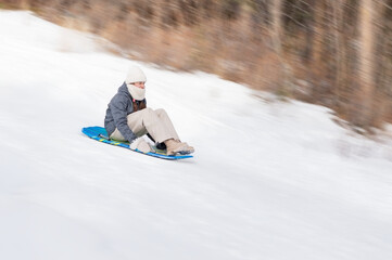 Girl sliding down snowy hill on foam sled side view