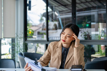 Fototapeta premium Businesswoman sitting at desk on couch in workplace or at home working on laptop and analyzing data on charts and graphs and writing on papers to make business plan and strategies for company.