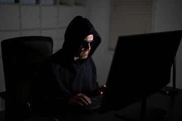 Digital thief. Hacker programmer in hoodie at office laptop, gaming. Hacker attack. Hacker gamer at night in office. Cyber attack. Cyber criminal and stolen personal data. Network exploit