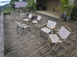 Group of empty outdoor folding chair furniture sit on rustic wood deck. peaceful and quiet scene, awaiting gathering with view of green mountain backdrop