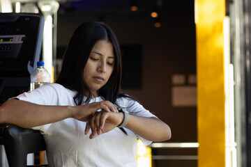 Young woman checking smartwatch while exercising at gym, monitoring fitness progress and training data for health technology and active lifestyle concepts