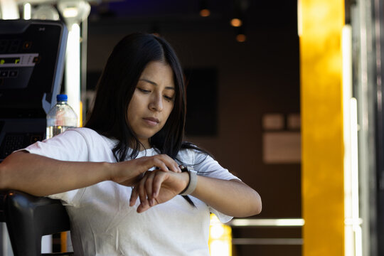 Young woman checking smartwatch while exercising at gym, monitoring fitness progress and training data for health technology and active lifestyle concepts