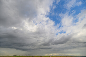 A Dramatic Cloudy Sky with Beautiful Blue Patches Above a Lush Green Landscape Below