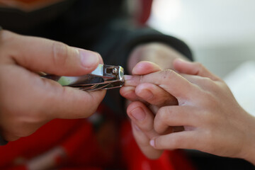 Obraz premium Adult hand gently using nail clipper to trim child small fingernail. This close up view shows moment of care, hygiene, routine, and grooming for personal health