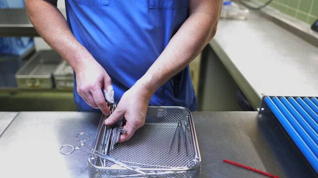 A healthcare worker in blue scrubs inspects and organizes surgical instruments in a sterilization tray inside a hospital reprocessing unit, ensuring cleanliness and patient safety.