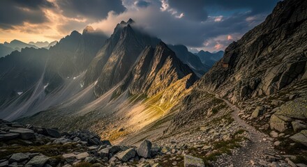 Rugged mountain peaks tower over a rocky hiking trail bathed in dramatic sunlight and shadow