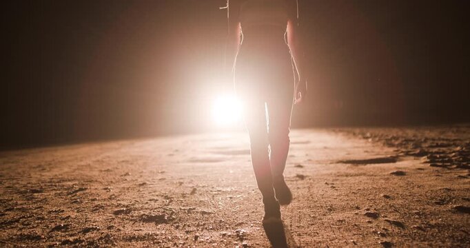 Girl walks in silhouette illuminated by car headlights on a dark road during night