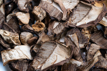 Earthy dried mushroom pieces scattered, Coarse broken caps and stems evoke woodland foraging, Sundried edges and porous surfaces suggest woodland harvesting scenes