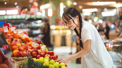 Young adult asian woman customer supermarket shopping cart choosing red apple fruits products grocery food at department store