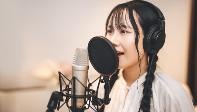 Asian woman vocalist with a microphone stand wearing headphones record singing song at home studio