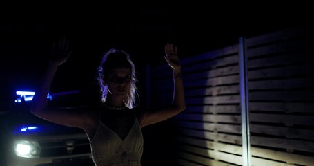 Girl with hands raised during police encounter at night in a secluded area with flashing lights