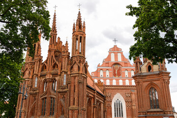The Church of St. Anne and the Bernardinai Monastery in Vilnius, Lithuania, 1 June 2025. Beautiful city streets on a sunny summer day. Historic buildings among green trees in a European city.