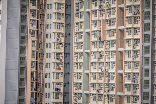 A high rise building with identical balconies and windows, many with air conditioners and drying clothes, showing city living conditions.