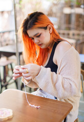 Asian happy beautiful cheerful outdoor portrait young woman light orange hair enjoying intend stringing beads is relaxing outdoors in urban cafe, activity joyful travel fresh nature holidays lifestyle