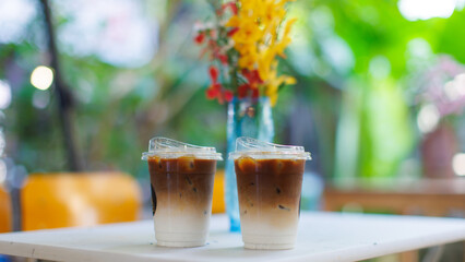 Yellow and red blooming bouquet flower arrangement in blue glass vase on white table and ice coffee, Natural tree cafe greenery create cozy rustic garden joyful fresh outdoor wooden chairs decorations