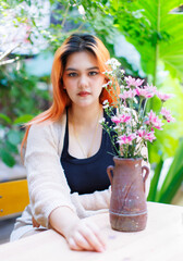 Asian happy beautiful cheerful outdoor portrait woman light orange hair smiling warmly among blooming bouquet flowers, Natural tree cafe greenery create cozy rustic garden joyful fresh nature concept