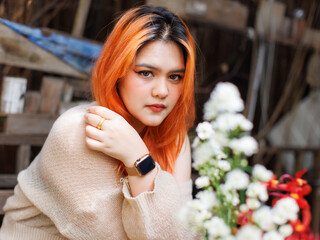 Asian happy beautiful cheerful outdoor portrait woman light orange hair smiling warmly among blooming flowers, Natural wooden textures greenery create cozy rustic garden joyful fresh nature concept.