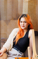 Asian happy beautiful cheerful portrait young woman light orange long hair smiling sitting art themed coffee shop cafe, natural wooden textures create joyful relaxation travel holidays lifestyle.