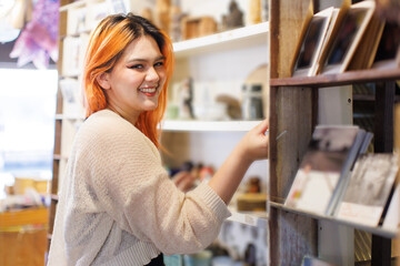 Asian happy beautiful cheerful portrait young woman light orange long hair smiling standing select to view handicrafts pottery shop on white wooden shelves joyful relaxation travel holidays lifestyle.