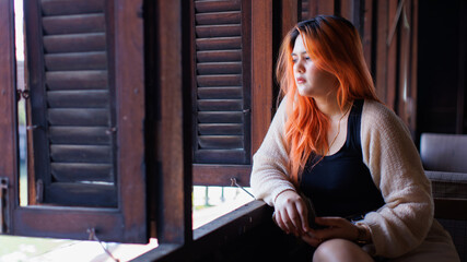Asian beautiful woman orange long hair smile wear black top cozy cardigan sitting look at view antique wooden window waterside village charming riverside background travel relaxation holiday.