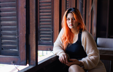 Asian beautiful woman orange long hair smile wear black top cozy cardigan sitting look at view antique wooden window waterside village charming riverside background travel relaxation holiday.