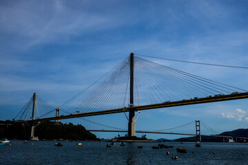 A scenic view of two bridges—one cable stayed and one suspension—spanning water with boats below and hills in the background.