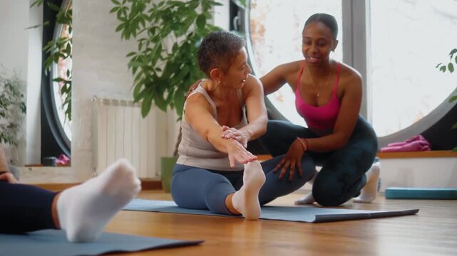 Positive energy and laughter during a stretching exercise as a Black female instructor supports an older senior woman, providing guidance and encouragement in a group fitness class.