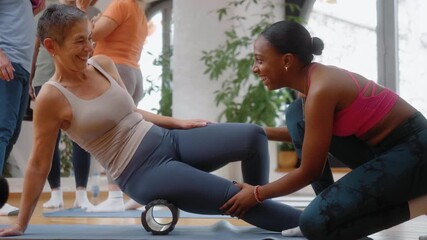 Black female instructor assisting an older woman during a foam roller exercise, creating a positive, relaxed, and joyful atmosphere in a senior group fitness class. - Powered by Adobe