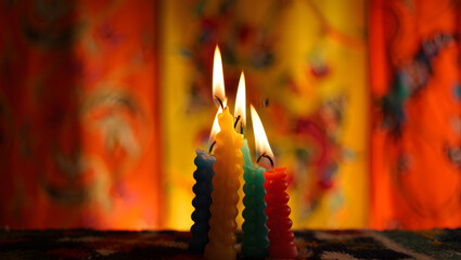 Three lit colorful candles with flickering flames in front of a warm background