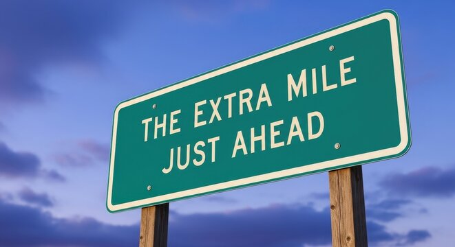 Green road sign displaying 'The Extra Mile Just Ahead' against a blue sky with clouds